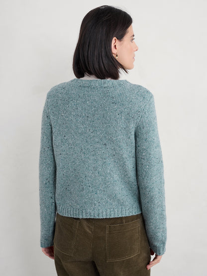 Person wearing a teal knitted cardigan against a plain background