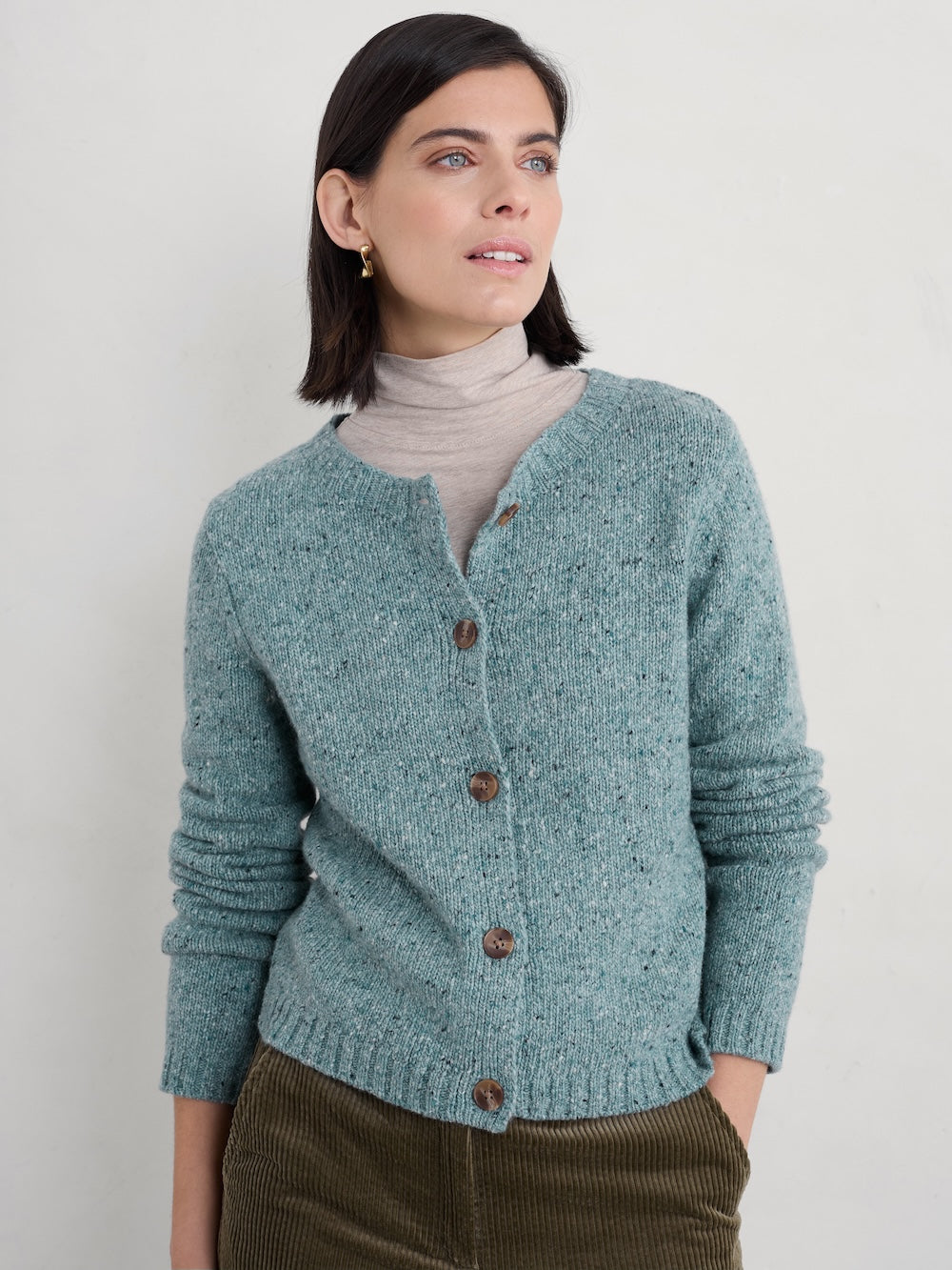Woman wearing a teal cardigan with brown buttons against a plain background