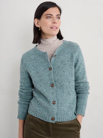 Woman wearing a teal cardigan with brown buttons against a plain background