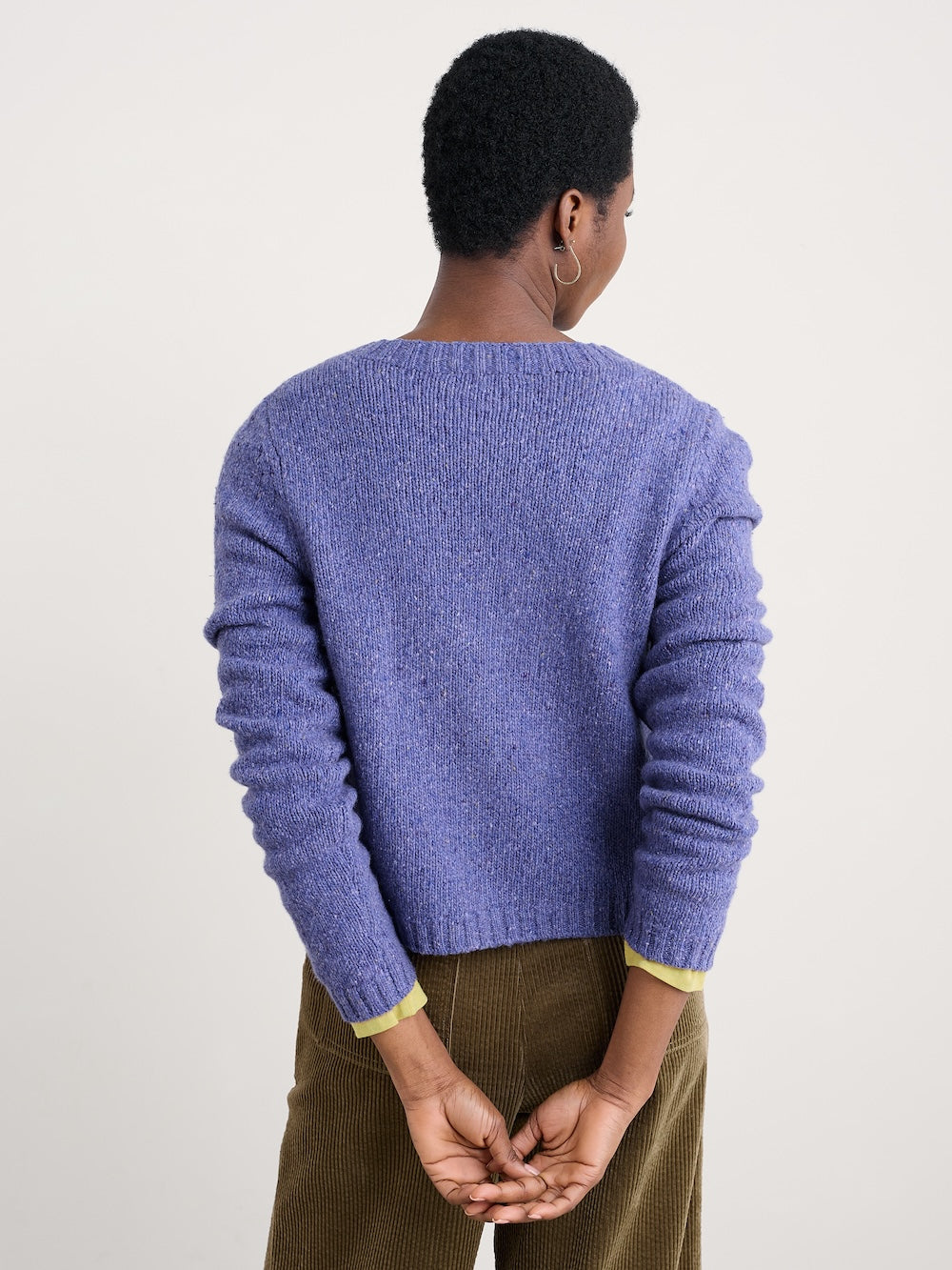 Person wearing a purple cardigan with a plain background