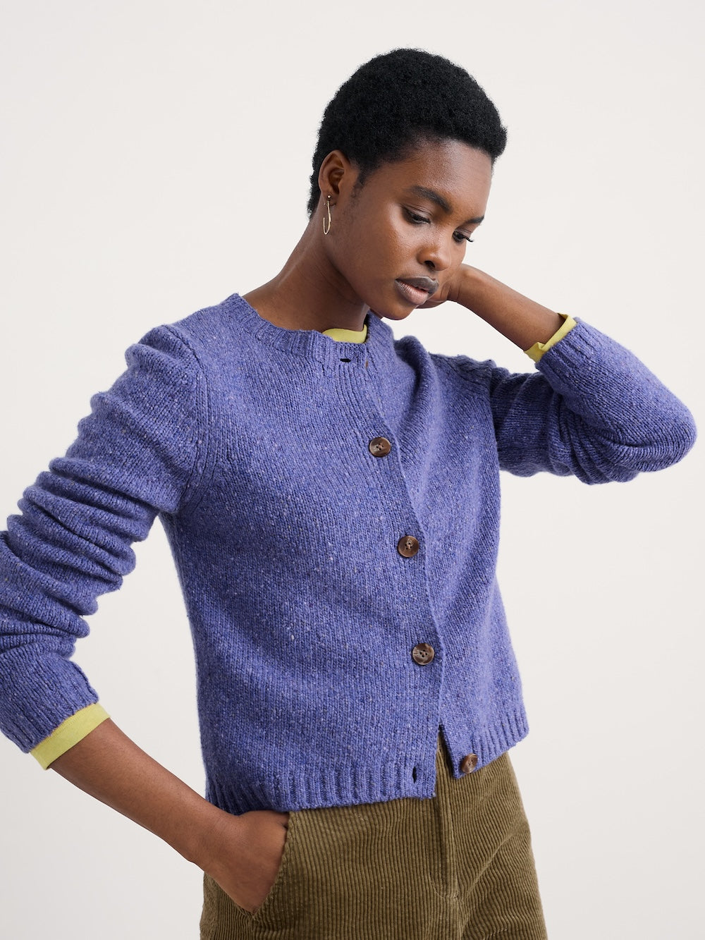 Person wearing a purple knitted cardigan with brown buttons on a plain background
