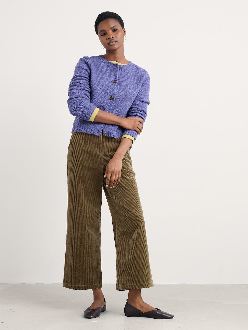 Woman wearing a purple cardigan and brown pants on a white background