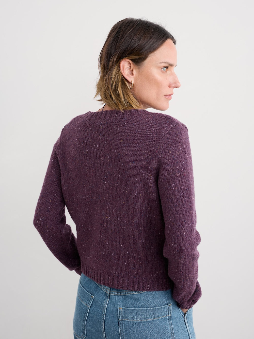 Woman wearing a purple cardigan and blue jeans against a white background
