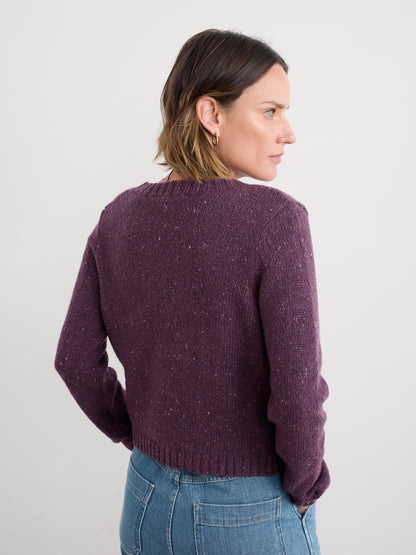 Woman wearing a purple cardigan and blue jeans against a white background