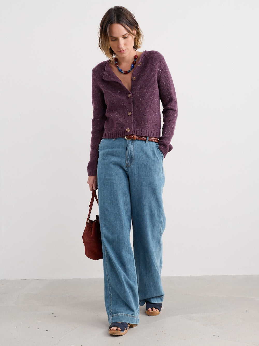 Woman wearing a purple cardigan and blue jeans, standing against a white background
