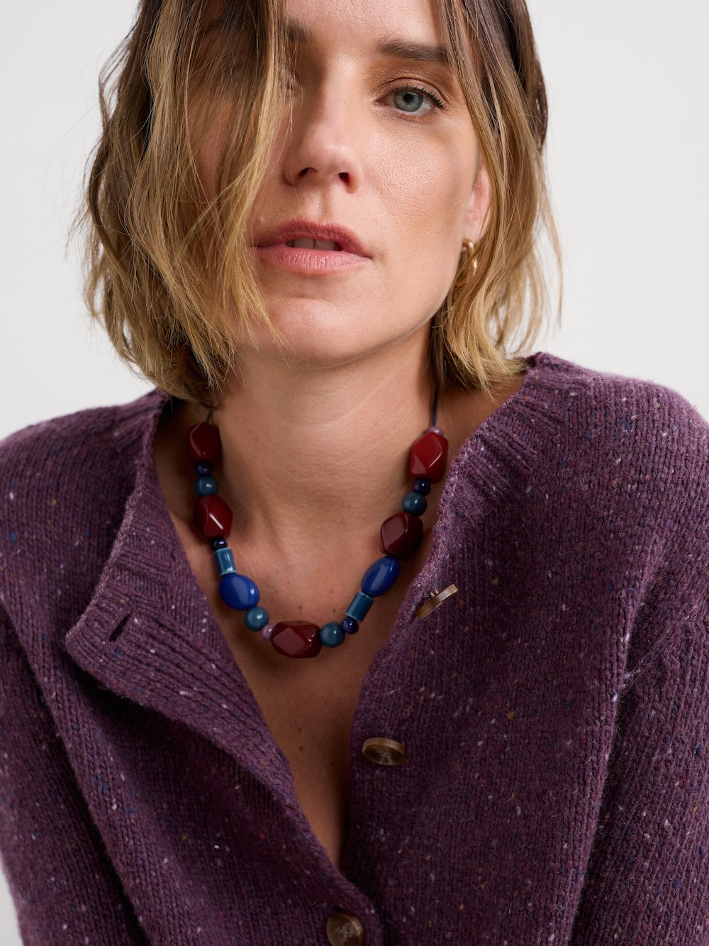 Woman wearing a purple cardigan and colourful necklace on a white background