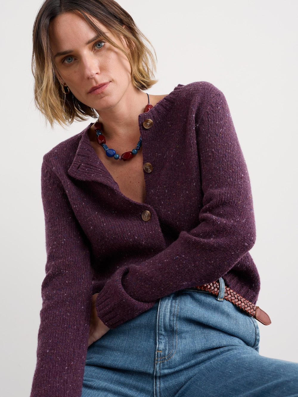 Woman wearing a purple cardigan and blue jeans against a white background