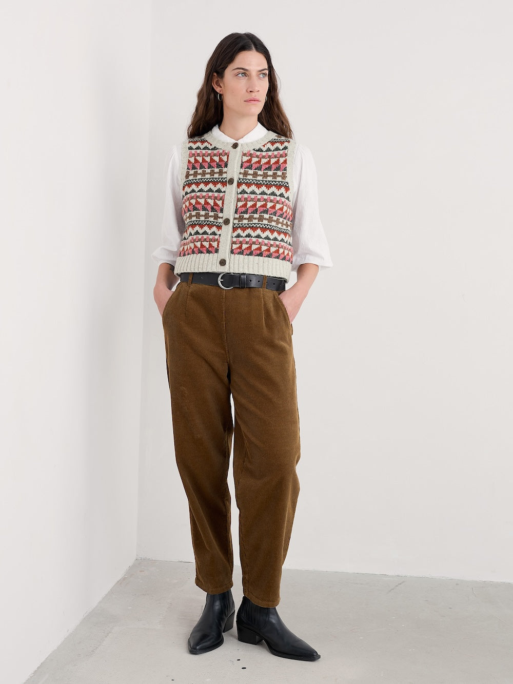 Person wearing a patterned sweater and brown pants against a white background
