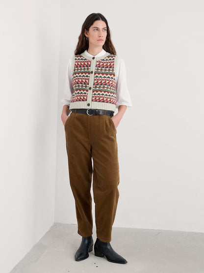 Person wearing a patterned sweater and brown pants against a white background