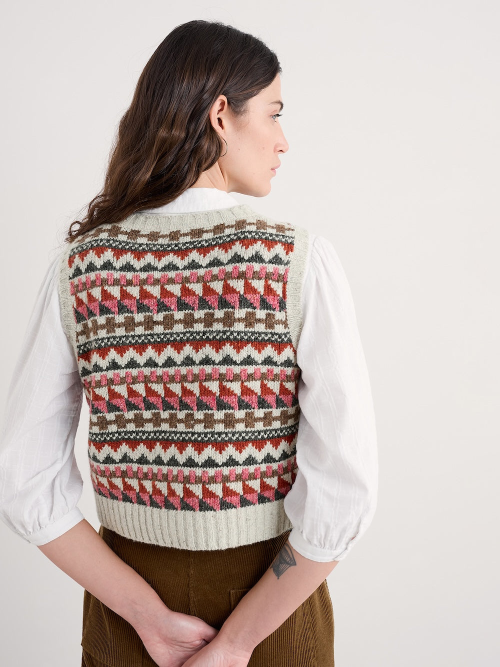 Woman wearing a patterned vest over a white shirt on a plain background