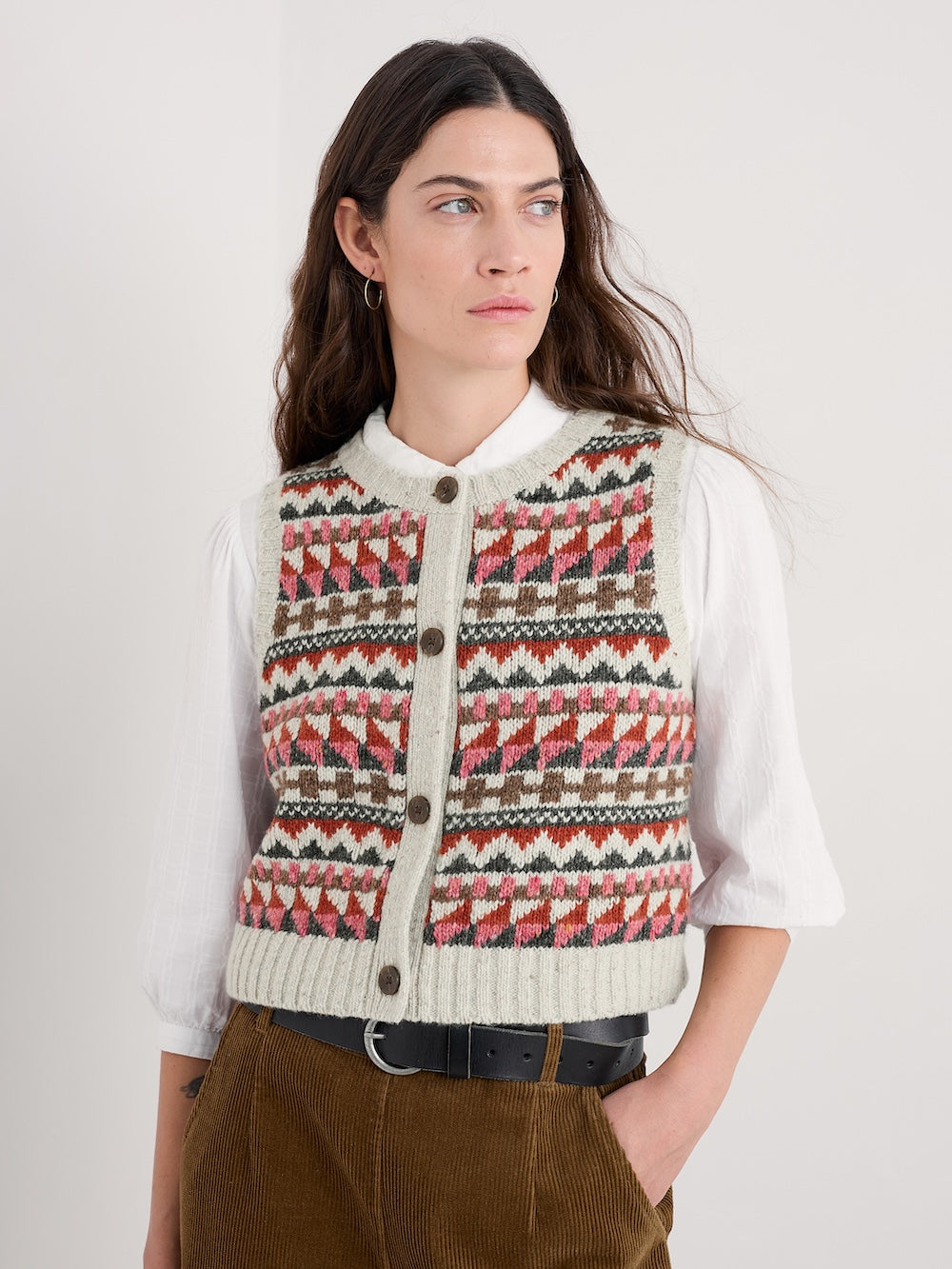 Woman wearing a patterned vest over a white shirt on a plain background