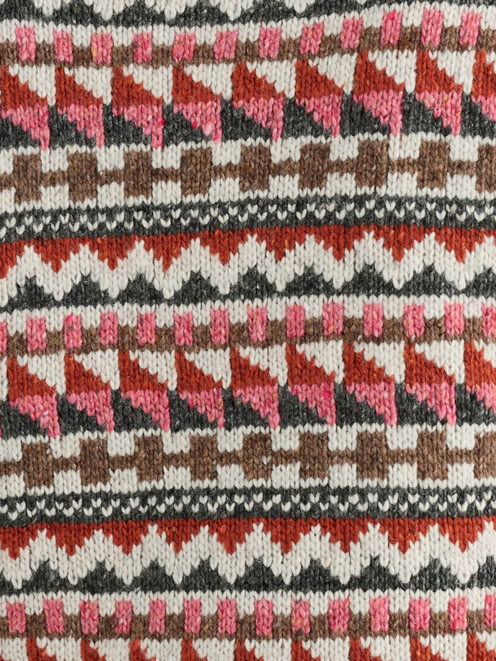 Close-up of a knitted fabric with a geometric pattern in red, pink, and brown.