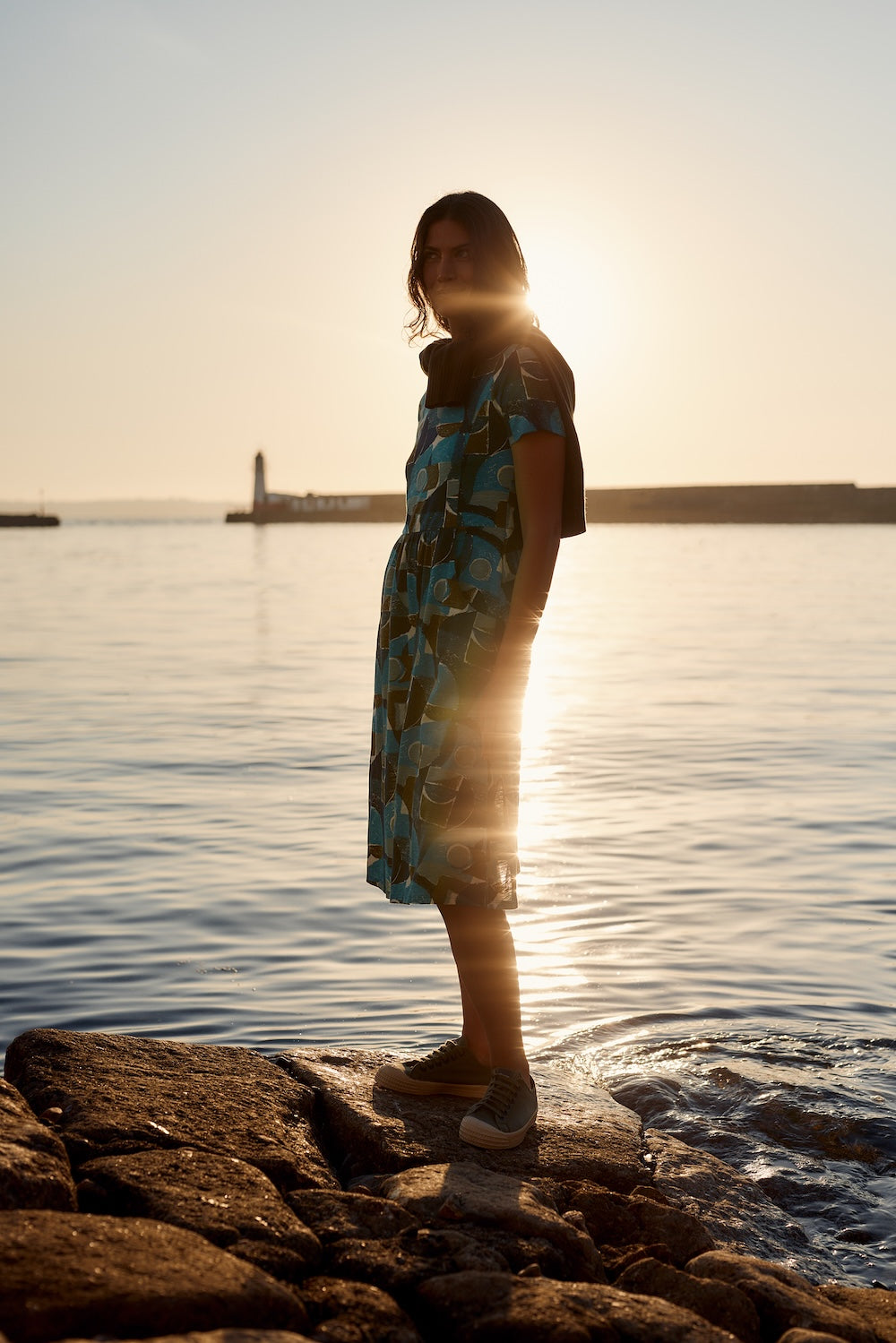 Person standing on a rocky shore with a sunset or sunrise over water