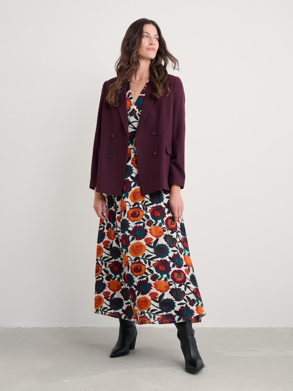 Woman wearing a floral dress and burgundy blazer against a white background