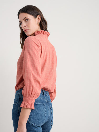 Woman wearing a coral blouse with a high collar and blue jeans on a white background