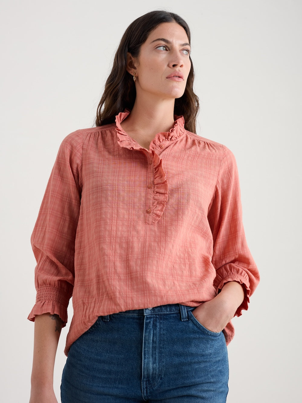 Woman wearing a pink blouse with ruffled details and blue jeans on a white background