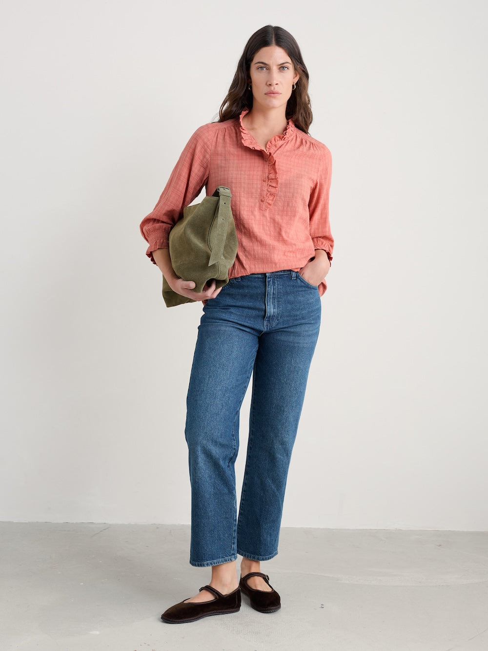 Woman wearing a pink shirt and blue jeans holding a green bag against a white background