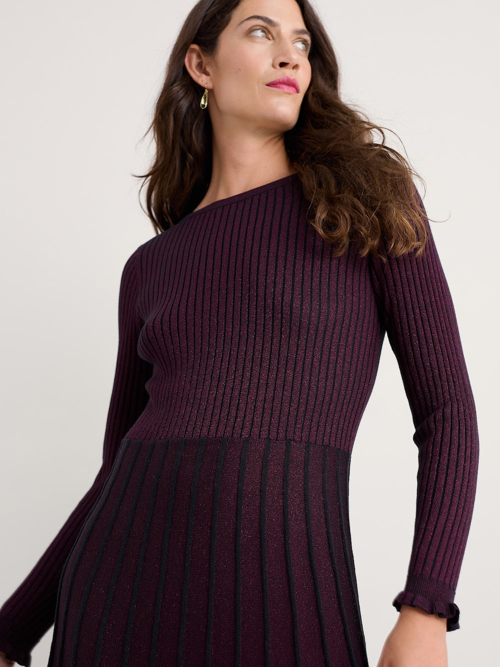 Woman wearing a dark purple ribbed dress against a plain background