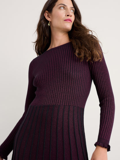 Woman wearing a dark purple ribbed dress against a plain background
