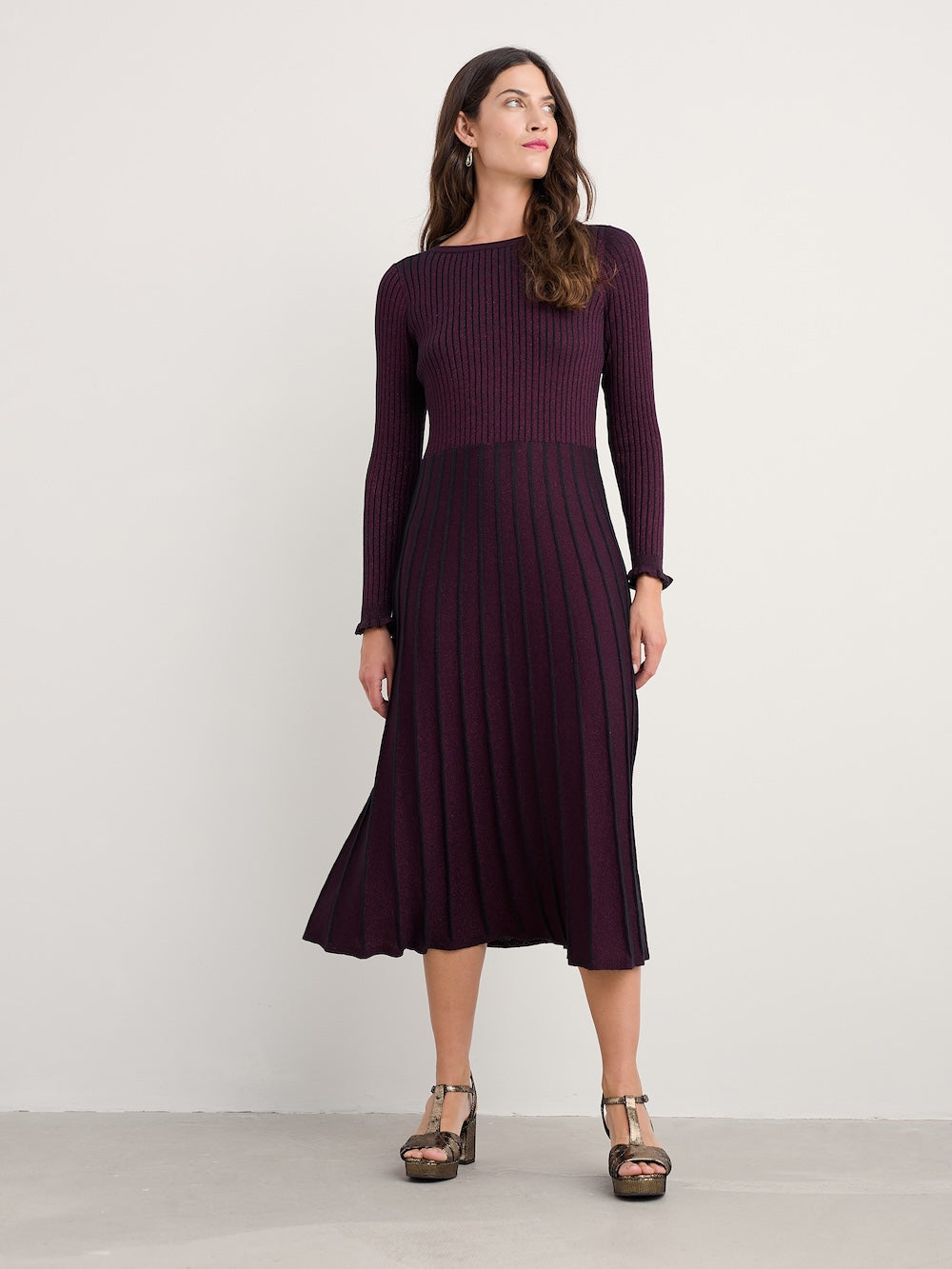 Woman wearing a long-sleeve, dark purple dress against a plain background