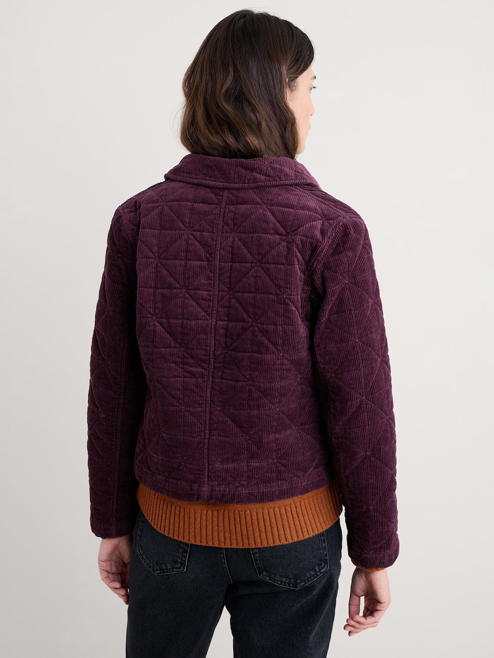 Person wearing a quilted purple jacket with a plain background