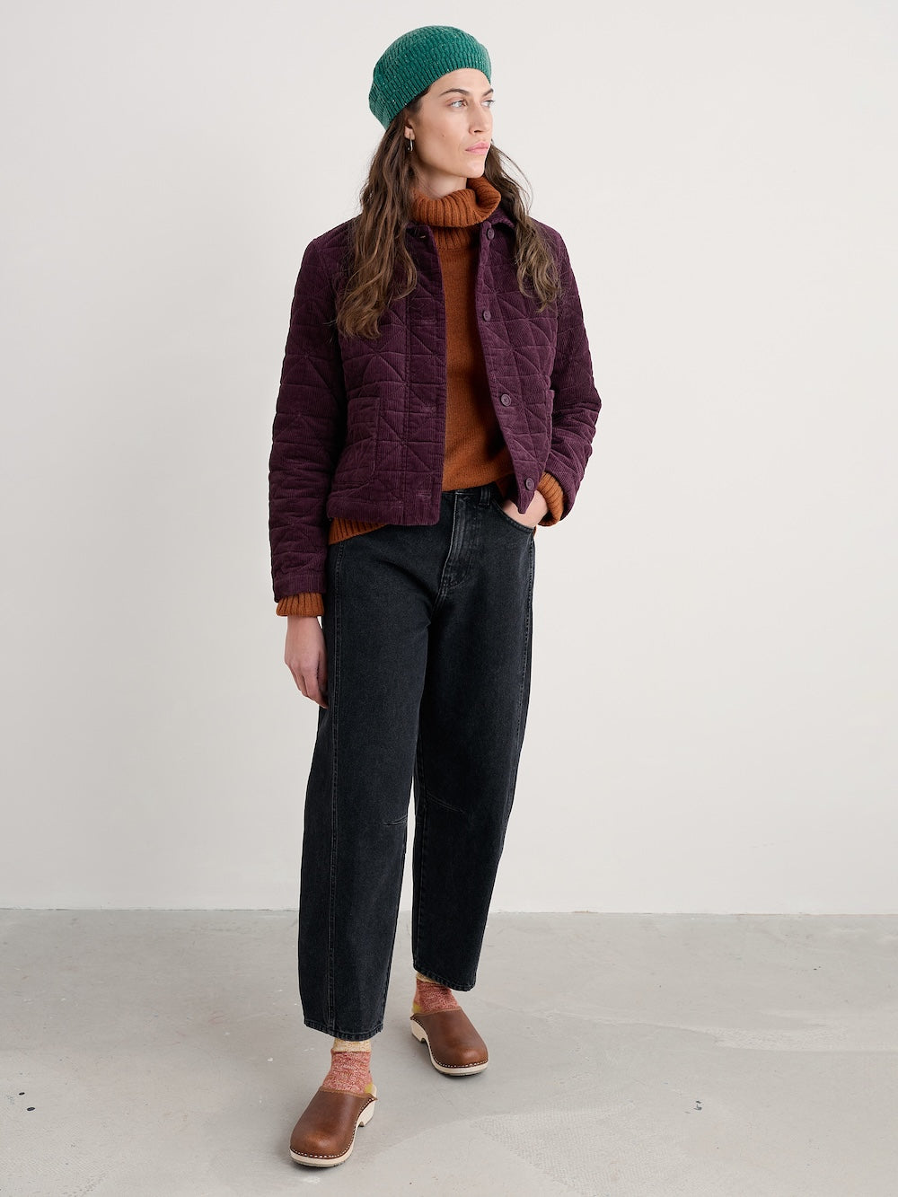 Person wearing a purple quilted jacket, green beanie, and black pants on a white background