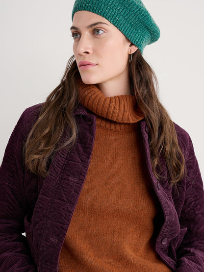 Woman wearing a green knit beanie and brown sweater with a purple jacket on a white background