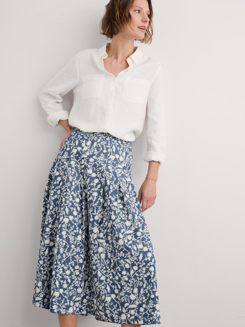 Woman wearing a white blouse and blue floral skirt against a plain background