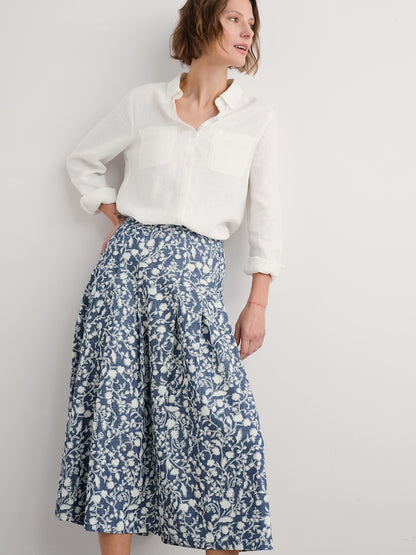Woman wearing a white blouse and blue floral skirt against a plain background