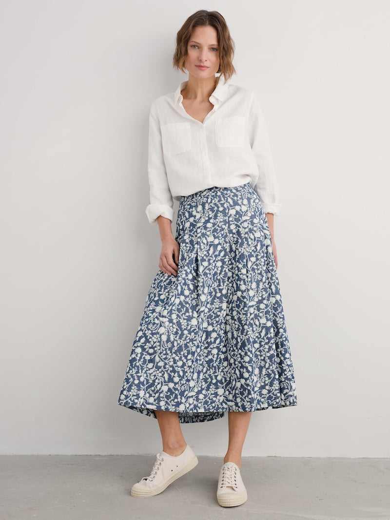 Woman wearing a white blouse and blue floral skirt on a plain background