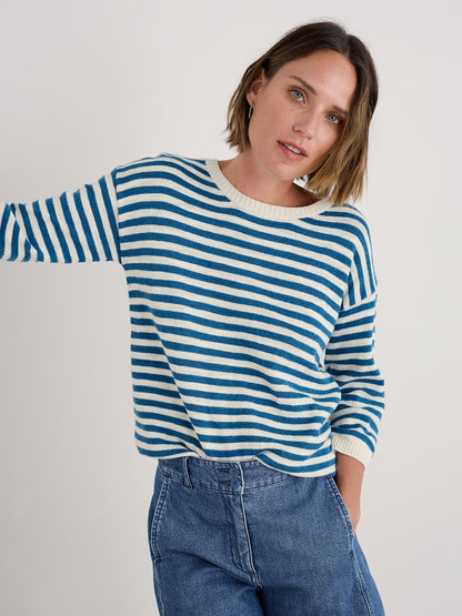 Woman wearing a blue and white striped sweater with jeans on a plain background