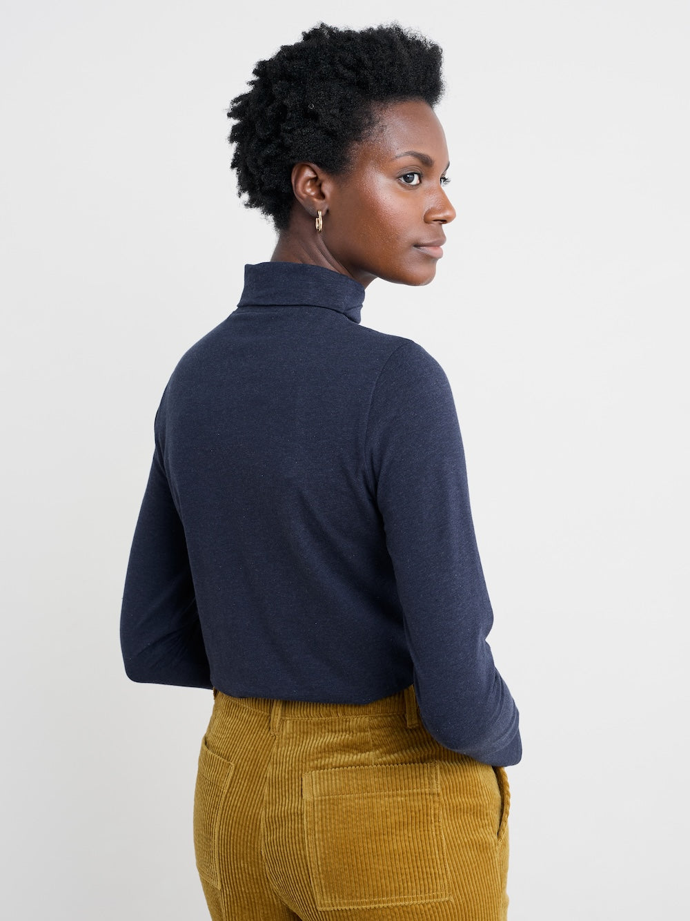 Person wearing a navy turtleneck and mustard yellow pants on a light gray background