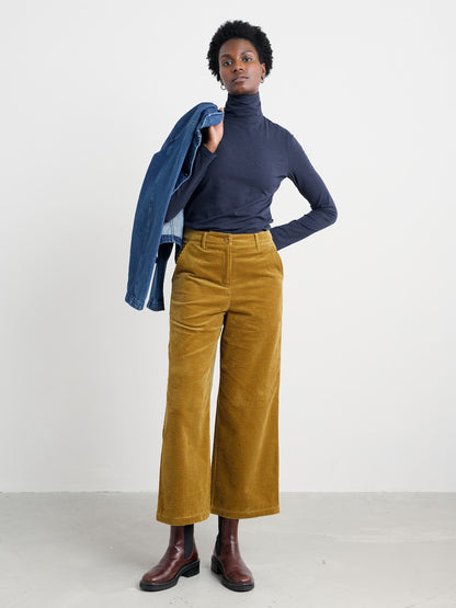 Person wearing a navy turtleneck, mustard yellow pants, and brown shoes on a white background