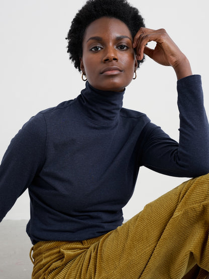 Woman wearing a navy turtleneck and mustard pants against a white background