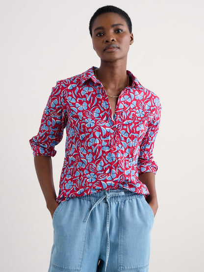 Woman wearing a red floral shirt and blue jeans against a white background