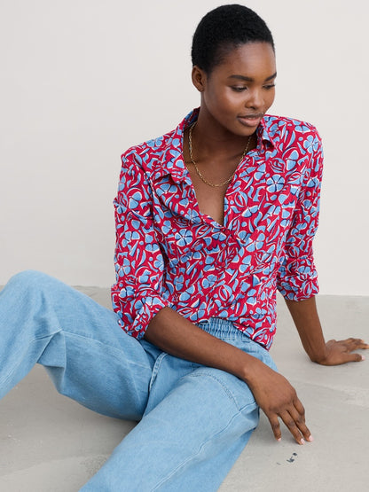 Woman wearing a red and blue floral blouse with light blue jeans sitting on a white floor.
