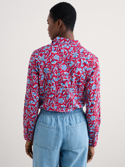 Woman wearing a red and blue floral patterned shirt with light blue pants on a plain background