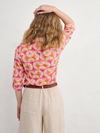 Woman wearing a pink and orange patterned shirt with beige pants on a white background