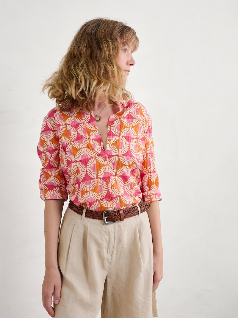 Woman wearing a colourful patterned shirt and beige pants on a white background