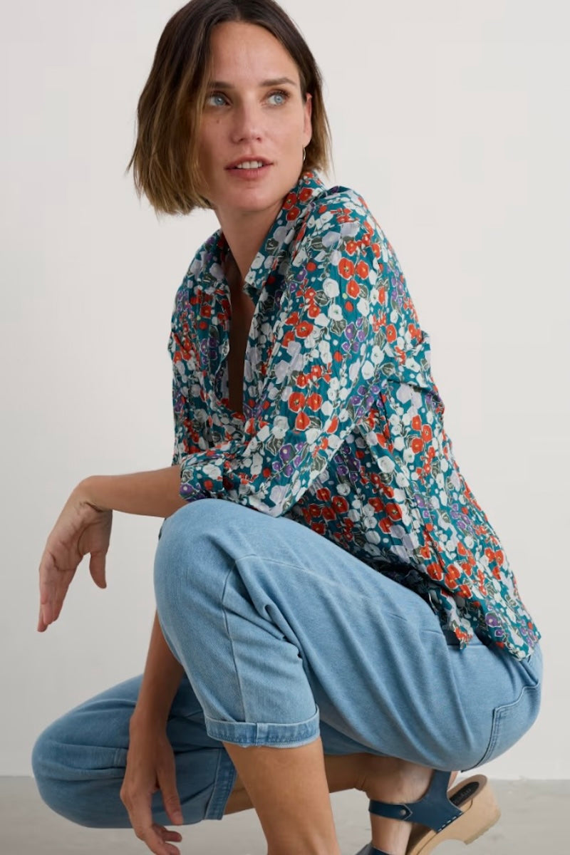Woman wearing a floral shirt and blue jeans sitting on the floor against a white background