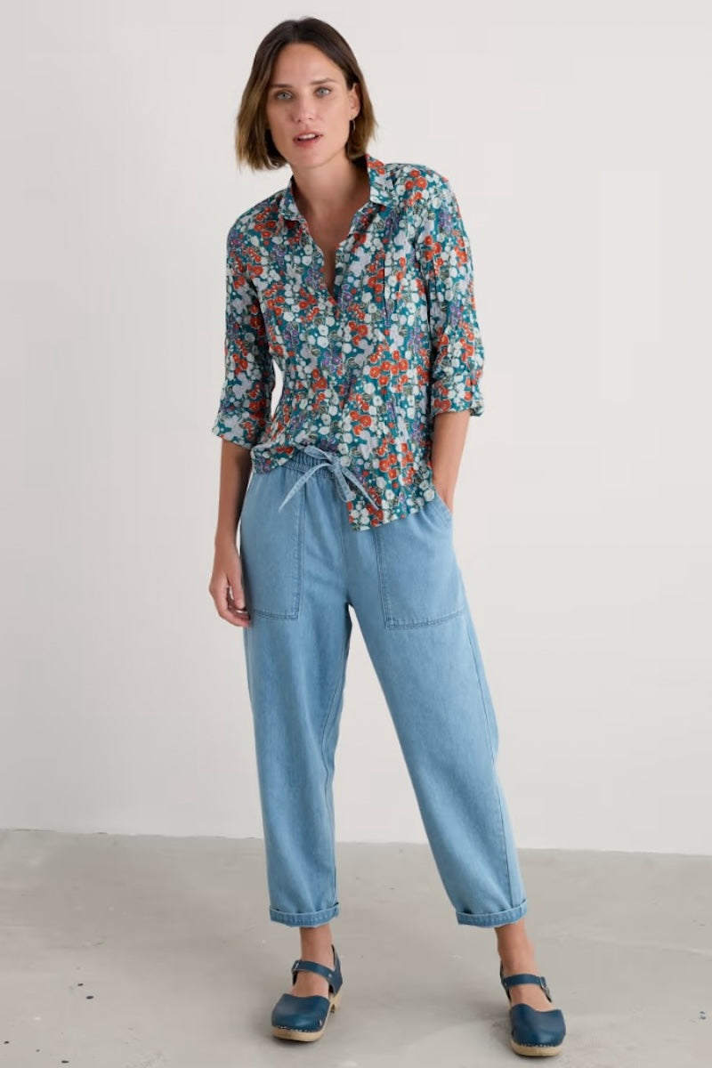 Woman wearing a floral shirt and light blue jeans against a plain background