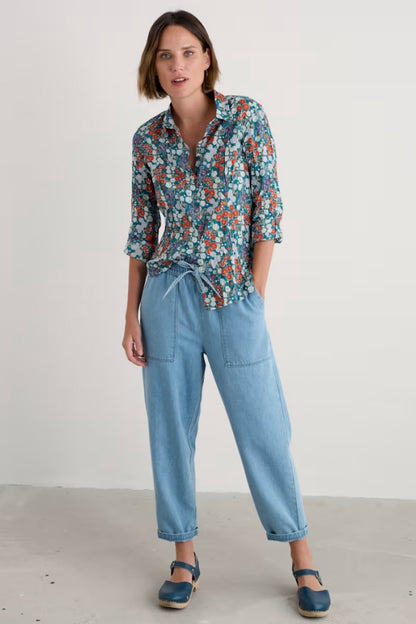 Woman wearing a floral shirt and light blue jeans against a plain background