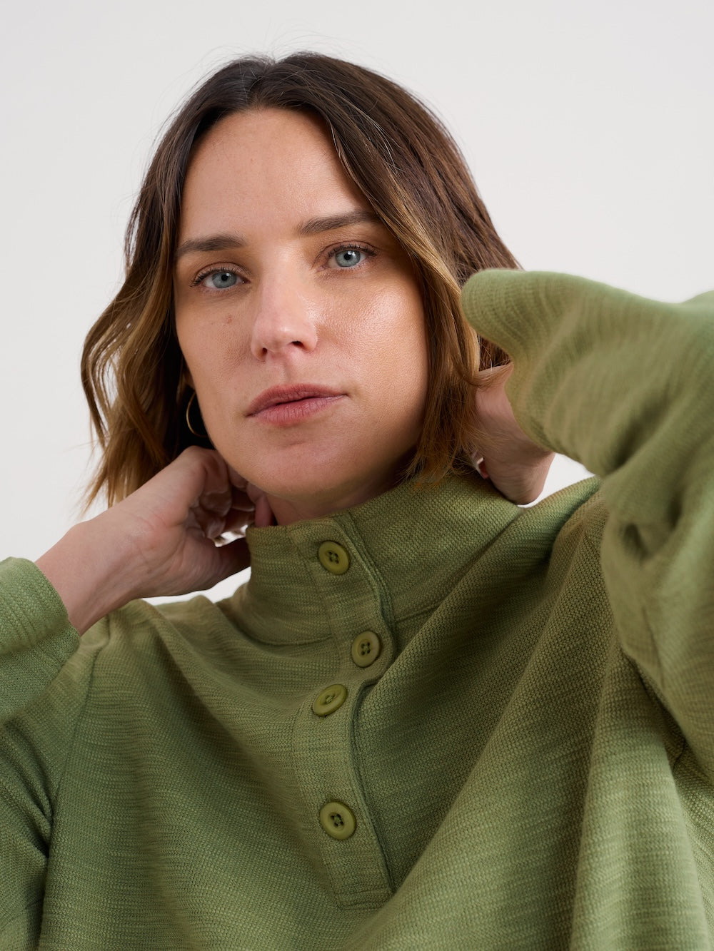 Woman wearing a green shirt with buttons, holding her sleeve up against a white background