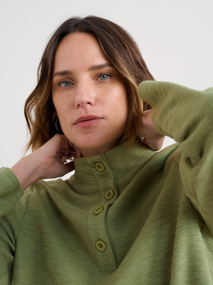 Woman wearing a green shirt with buttons, holding her sleeve up against a white background