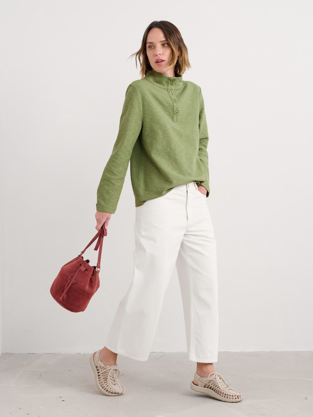 Woman wearing a green shirt and white pants, holding a red bag on a plain background