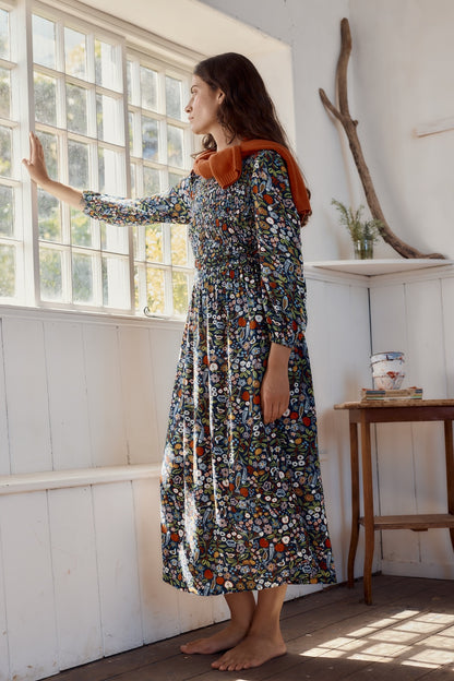 Woman in a floral dress standing by a window in a bright room.