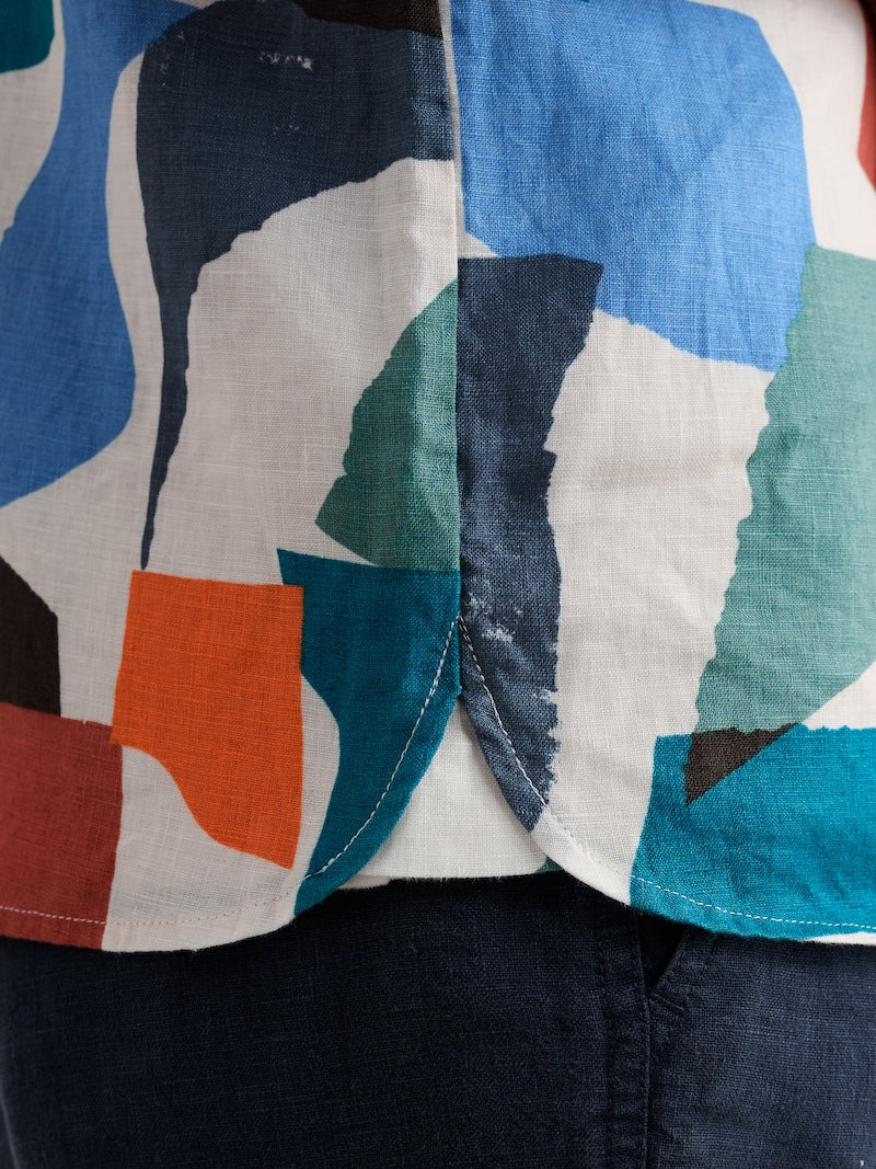 Close-up of a colourful shirt with abstract patterns in blue, green, orange, and black on a white background.