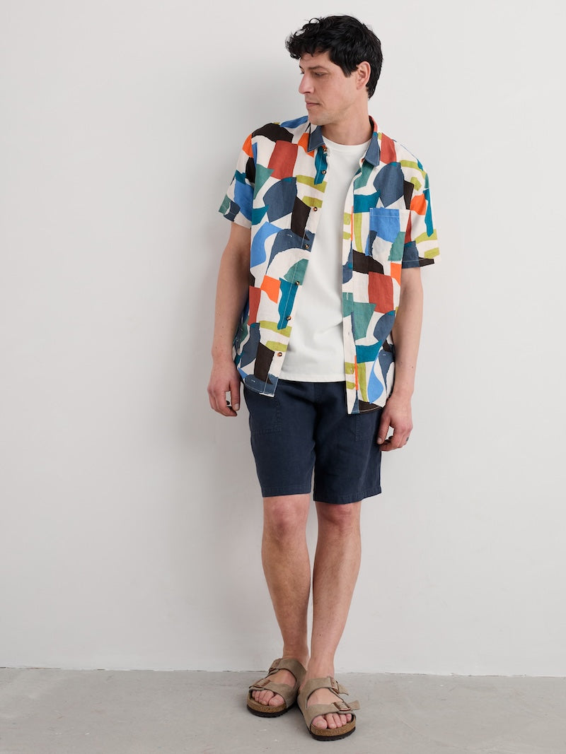 Person wearing a colourful geometric-patterned shirt and navy shorts against a plain background