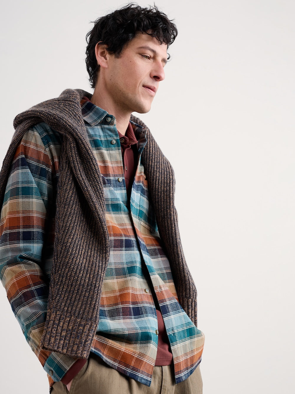 Man wearing a plaid shirt and brown jumper against a white background