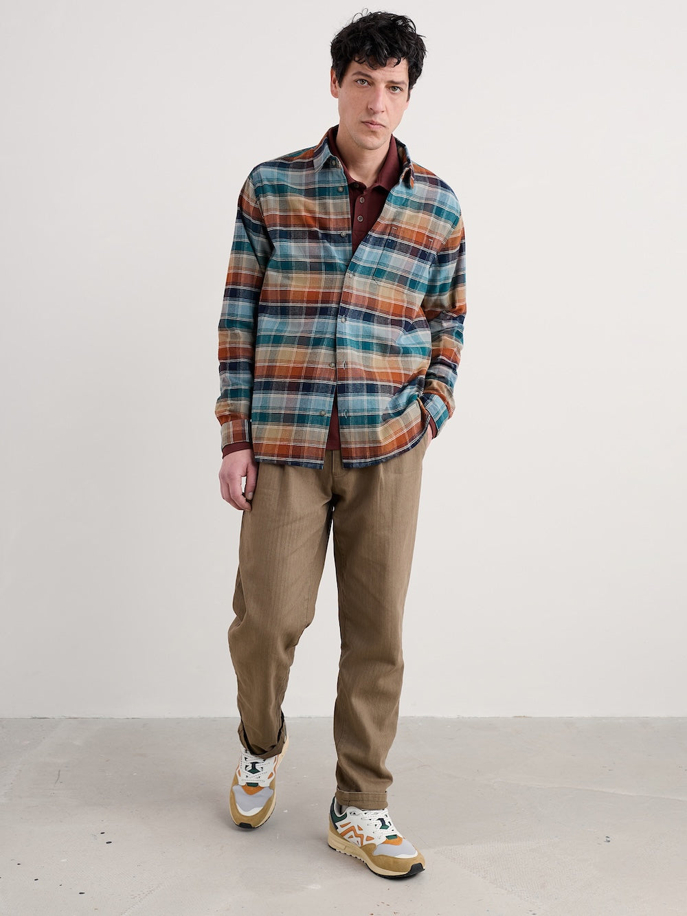 Man wearing a plaid shirt and brown pants against a white background